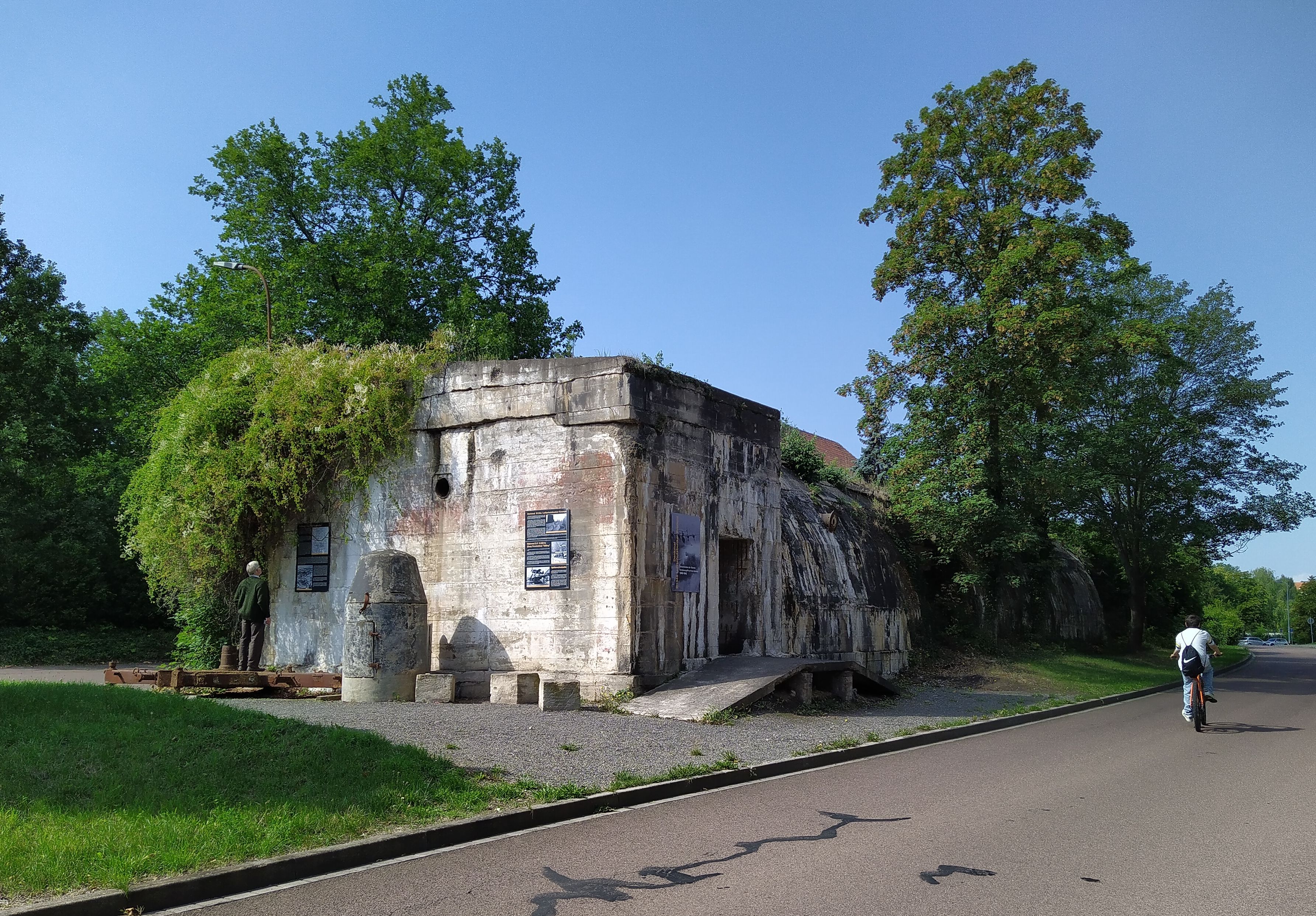  Road, Architecture, Building, Bunker, Person, Tarmac, Plant, Tree, Backpack, Bag, Bicycle, Transportation, Vehicle, Outdoors, Shelter, Car, Clothing, Footwear, Shoe, Nature, E-scooter, City, Street, Urban, Accessories, Handbag